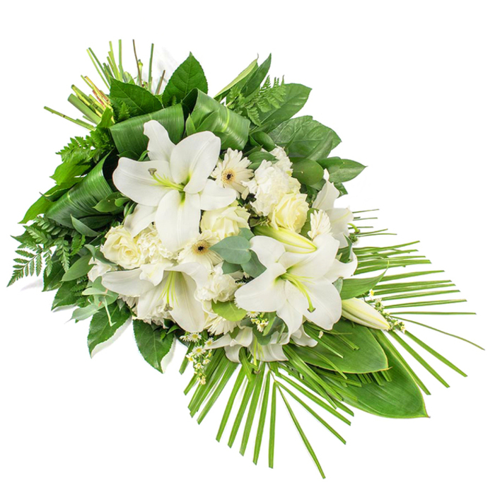 An elongated white and green funeral spray is presented diagonally on a crisp white background, its form reminiscent of a cascading teardrop gently flowing from left to right. Central to the display are several grand white Oriental lilies, some fully opened to reveal their trumpet-shaped blooms with yellow-green stamens, others still in graceful bud, adding height and anticipation. Around them, clusters of soft white roses gather, from tightly folded buds to partially opened blooms that show their many delicate layers. Interspersed among the roses are ruffled white carnations and daisy-like white Gerberas, each bloom with a subtle cream or darker centre, bringing a touch of brightness and a modern edge. Tiny white filler flowers, such as gypsophila or waxflower, are scattered throughout the arrangement, forming a fine, airy veil that softens the transitions between blossoms. The spray's shape is defined by a rich framework of greenery, building a long, one-sided composition ideal for placing at the head of a coffin or on a stand in a Brent Cross chapel of rest. Glossy dark green leaves form a solid, supportive base; light, feathery ferns add an almost whisper-like movement; and rounded eucalyptus leaves, with their muted green-blue tones, lend subtle colour variation and a hint of fragrance. At the top of the design, long, narrow leaves are carefully folded and bound, adding a vertical emphasis and suggesting skilled craftsmanship. From the lower right, a fan of slender palm fronds sweeps outward, extending the arrangement's silhouette and giving it a contemporary, flowing character. The cool whites and fresh greens together communicate purity, remembrance, and quiet serenity, making this tribute especially fitting for families in Brent Cross seeking a refined, heartfelt expression of farewell.