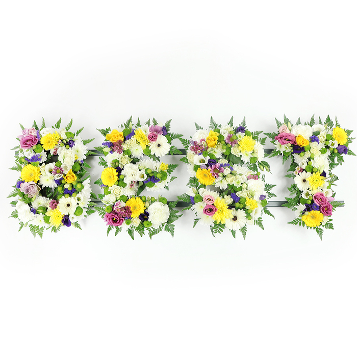 A striking, professionally crafted floral tribute photographed straight-on, the four large letters spelling BEST formed from a lush, tightly packed mix of fresh flowers and deep green ferns set against a clear white studio background. The arrangement reads with warm clarity: dominant sunny yellows from roses and gerberas pair with clean white, multi-petaled chrysanthemums to create a bright, consoling surface. Accents of gentle lavender-purple lisianthus and vibrant magenta spray roses or carnations weave through the composition, offering depth and a sober, elegant contrast. Fine clusters of pale green and ivory filler flowers sit low between the larger blooms, supplying delicate texture and soft transitions from one bloom to the next. The fern fronds trace and soften the outer edges of each letter, their natural curve framing the type like a wreath of living green.

Carefully engineered, the letters reveal a dark green or subtle metal frame in a few tight gaps - most noticeably under the E's middle bar and along the lower edge of the T - evidence of the discreet support needed for a display of this scale. The lighting is bright and even, revealing the tactile detail of each petal and the slight sheen of freshly cut leaves. The overall mood is one of tender respect and quiet celebration, the word BEST offering a personal, heartfelt message at a funeral or memorial, or mounted at a celebration of life. As local florists at Brent Cross Flowers, we often craft similar letters for families across Brent Cross, Hendon and Temple Fortune who seek a clear, heartfelt floral message rendered with careful craftsmanship and garden-fresh blooms.
