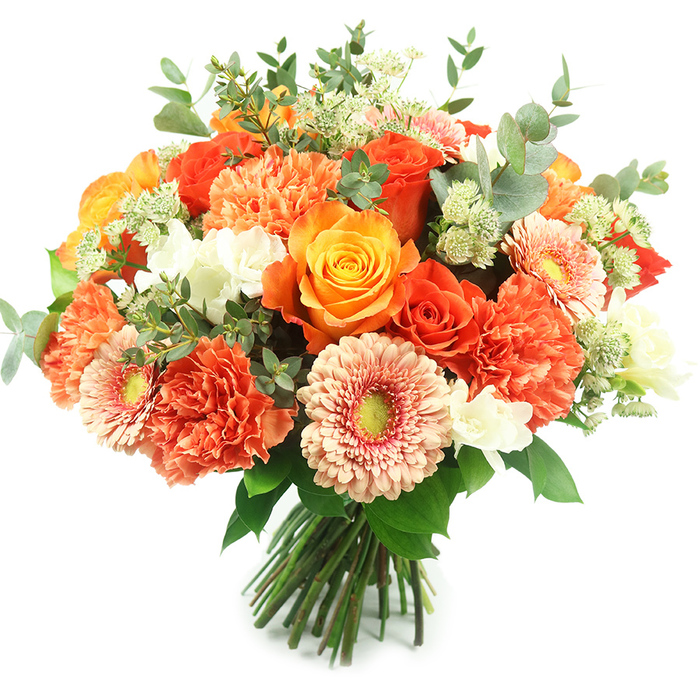 A luxurious, generously packed hand-tied bouquet is shown against pristine white, its rounded form full of layered colour and texture that reads like a warm embrace. At the centre, several large roses-ranging from deep, fiery orange to a luminous golden-yellow-display tightly swirled petals and varying stages of bloom, creating thoughtful depth and focal drama. Surrounding them are plentiful coral and burnt-orange carnations, their frilly, multi-layered petals forming soft clouds that add volume and tactile richness. Interspersed with these are soft peach gerbera daisies, each with a luminous face and a slightly recessed yellow-green eye that introduces a playful yet elegant counterpoint. Bright, small white filler blooms, resembling freesia or tiny spray carnations, are sprinkled throughout to lift the warmer palette and provide crisp highlights. Delicate clusters of light green, astrantia-like filler contribute a feathery texture that dances above the main flowers, while abundant eucalyptus leaves in a muted silvery-grey-green are woven through the bouquet to give structure, cool contrast and a faint aromatic note. The stems are tightly gathered and tied, visible at the base, evidencing professional hand-tying and a bouquet ready to be placed in a vase. Bathed in soft, even light, this arrangement communicates celebration, gratitude and refined warmth-an ideal choice for autumn events, birthday centrepieces or thoughtful gifts. The composition also carries a local sensibility, the kind of balanced, seasonal design a neighbourhood florist might prepare for clients around Brent Cross, Cricklewood and the nearby shopping precincts seeking a confident and elegant floral statement.