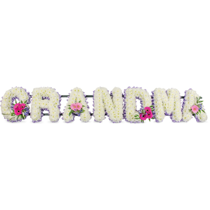In the photograph, the word GRANDMA is presented as a floral tribute in large, evenly spaced letters, the kind of arrangement that might be gently carried from a Brent Cross home to a quiet service nearby. Every letter is densely covered in white chrysanthemums, their blooms so tightly clustered that they create a continuous, velvety surface. The petals curve softly outward, giving the whole piece a cushioned, almost quilted appearance, as if meant to embody comfort and embrace. The white flowers symbolise peace and remembrance, and their pristine condition suggests they have been freshly prepared, ready for same-day delivery across the local area. Encircling each letter is a fine edge of lilac ribbon, carefully pinned in place, following the contours with tidy precision. The ribbon's gentle colour adds refinement and a delicate sense of femininity, perfectly suited to a tribute for a cherished grandmother who may have shared stories and tea around the Brent Cross Shopping Centre or nearby residential streets. At three thoughtfully chosen points along the tribute-the opening G, one central A, and the final A-clusters of brighter flowers break through the white. Each cluster features pink gerbera daisies with open, daisy-like faces, petite pink roses at varying stages of bloom, and sprigs of fresh greenery that arch slightly outward. These accents bring movement, life, and contrast, suggesting the lively character and loving presence often associated with a grandmother. Soft, diffused lighting illuminates the arrangement, making the textures of petals, leaves, and ribbon clearly visible without glare. The overall impression is one of tenderness and gratitude, a floral message of love and farewell expressed with care and craftsmanship.