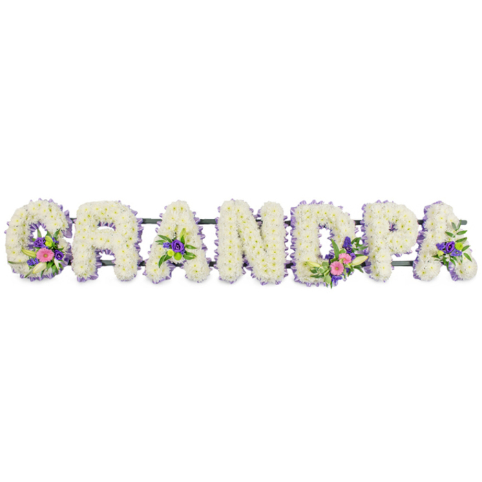 A personalised funeral flower arrangement spelling out the word GRANDPA stretches from left to right, designed as a meaningful tribute for a grandfather's farewell in Brent Cross or the surrounding North London suburbs. The seven bold letters are constructed on sturdy frames and then completely covered with compact clusters of white chrysanthemums, or similar classic funeral blooms, each head carefully angled so that the surface appears even, soft, and luxuriously full. Around the outer edge of every letter, the florist has added a slender trim of lilac and light purple blossoms, likely statice or small asters, which frame the white base with a mists of colour, emphasising the shapes and making the name easy to read from a distance in a crematorium or cemetery chapel. The otherwise uniform white is gently broken by a few well-placed accent clusters: in the G, a spray of vivid pink flowers and an elegant white lily-like bloom sit among deep green foliage, creating a focal point. The first A and final A are each adorned with smaller groupings of rich purple florets and leaves, while the D carries a more noticeable cluster that mirrors the G, combining pink, fuchsia, and white with refreshing greenery and occasional bright green button chrysanths. All seven letters are aligned on a long, narrow dark green support bar that runs behind them, mostly hidden, but essential to keeping the tribute straight for display beside a coffin, at the front of a church, or on stands at a graveside gathering near Brent Cross. The clean, all-white background and soft, even lighting allow every detail of the flowers to be appreciated, highlighting the care, precision, and artistry that went into the design. Crafted in the style often requested from Brent Cross Flowers, the tribute feels deeply personal and respectful, offering a quiet, floral expression of love, memory, and gratitude for a cherished family patriarch.