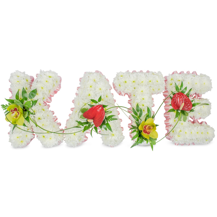 In this image, the name KATE is lovingly rendered in four distinct floral letters, each one resting against a plain white background that allows the tribute to take centre stage. The structure of every capital letter is composed of tightly grouped white chrysanthemums, their neat, rounded petals overlapping to form a full and velvety surface. This dense bed of blooms gives the letters a soft, inviting texture that speaks of peace, purity, and gentle remembrance. The outer edges are finely trimmed with pale pink satin ribbon, gathered into delicate folds that create a light, frilled border, adding a feminine charm and a hint of colour without overwhelming the calm white base. At thoughtfully chosen points, vibrant accent flowers and greenery provide contrast. On the K and at the bottom of the T, lime-yellow cymbidium orchids with deep red markings are nestled among glossy dark leaves and feathery fern fronds, giving the design depth and a sense of luxury. The A and E carry a single red anthurium each, their heart-shaped, waxy petals glowing against the white chrysanthemums and symbolising love that endures beyond farewell. Thin green tendrils weave gently across the arrangement, linking the letters with a natural, flowing line that suggests connection and continuity. The tribute feels bespoke and heartfelt, ideal for a funeral, memorial service, or celebration of life in and around Brent Cross, perhaps near local chapels, community halls, or quiet corners of nearby parks. It evokes the careful touch of an experienced local florist who understands the importance of creating a floral memorial that truly reflects the person being remembered.