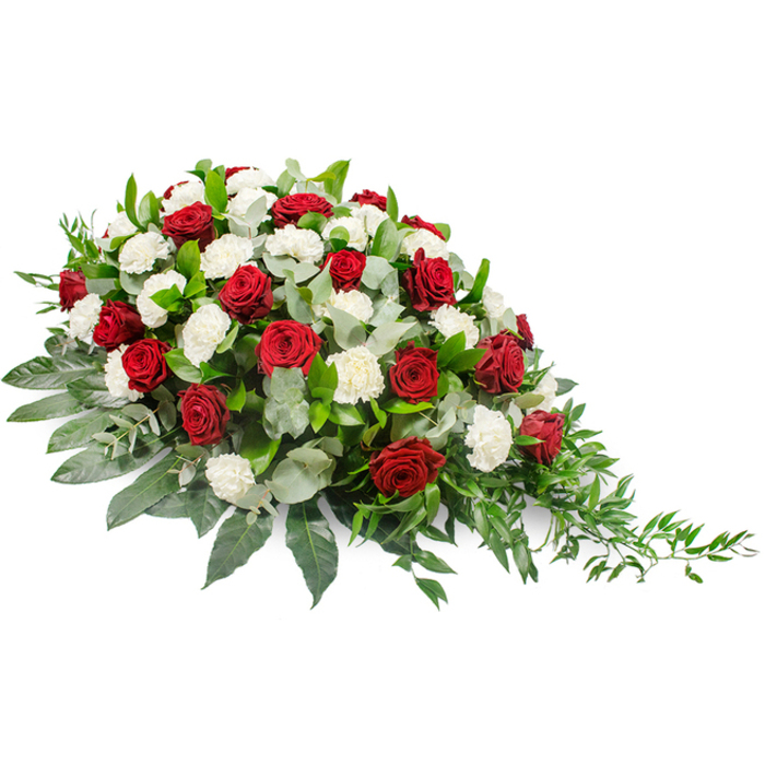This photograph captures a traditional funeral spray in rich, contemplative tones of deep red, white, and green, carefully arranged on a stark white background so that every stem and petal is clearly defined. The design has a horizontal, slightly asymmetrical form: its left side is full, rounded, and mounded, then gradually thins to a fine, tapering point on the right, evoking the image of a single, elongated teardrop. Scattered throughout the spray, deep crimson red roses stand slightly proud of the other flowers, their petals tightly wrapped and velvety, conveying profound affection, reverence, and the weight of farewell. Between them shimmer the softer forms of white carnations, with their layered, frilled petals creating a plush, cloud-like texture. The interplay of crimson and white suggests both the intensity of grief and the hope of peaceful rest. Supporting this floral story is a base of lush greenery. Dark, broad leaves form a solid, glossy foundation, giving the arrangement a well-anchored look, while muted, silvery-green eucalyptus leaves curve and twist among the blooms, adding a gentle, cool-toned contrast and a sense of depth. At the far right tip, delicate, trailing sprigs of lighter green foliage extend outward, softening the angle and adding a touch of natural grace, reminiscent of foliage drifting over the banks of the nearby River Brent. A piece like this would be chosen for a funeral service or crematorium ceremony in and around Brent Cross, perhaps travelling quietly from a family home near the shopping precinct or along the North Circular. It feels like a carefully considered tribute, designed to lie along a casket or at the front of a chapel, offering colour, fragrance, and a visual expression of love when words are hard to say.