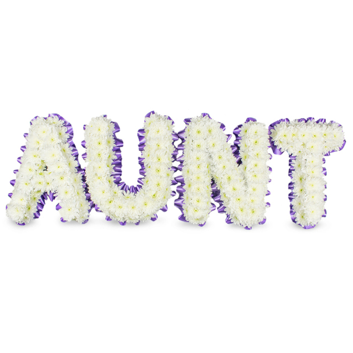 A meticulous, close-framed study of a memorial tribute that spells 'AUNT' in bold capital letters made entirely from pristine white spray chrysanthemums, their small, abundant petals layered densely to create a plush, almost cloudlike texture across each letter. Some blooms reveal soft yellow hearts, tiny points of warmth within the white field, while a deep purple satin ribbon scallops delicately around each perimeter, ruffled against the letter frames so the ribbon's sheen and texture read clearly beside the matte softness of the chrysanthemums. The composition sits on a pure white surface and is lit to produce delicate grey shadows beneath each letter, giving the work a palpable three-dimensional feel and a sense of measured presence. The design conveys both reverence and gentle celebration: the cool, clean whites suggest purity and remembrance, the purple edge brings a measured dignity, and the whole reads like a floral embrace. You can almost sense a faint, green, dewy fragrance rising from the blooms - a subtle sensory layer that complements the visual calm. As a local tribute this would suit funerals and memorial gatherings across Brent Cross, Hendon and surrounding wards, where families often choose personalised letter tributes for an intimate farewell. The arrangement communicates skillful workmanship, considered materials and an intention to honour a beloved aunt with both beauty and restraint.
