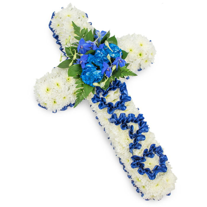 A classic funeral flower cross dedicated to a father is displayed against a pure white background, evoking the feeling of a freshly finished tribute in a Brent Cross Flowers workshop, awaiting delivery to a nearby chapel or crematorium. The long, symmetrical shape of the Christian cross is entirely blanketed with white spray chrysanthemums, the blooms arranged so closely together that they form an almost seamless, pillow-like expanse. Each chrysanthemum head is small but full, with layered petals that lend a soft, velvety texture to the arrangement, symbolising peace and gentle remembrance. Around the outer edge, a royal blue satin ribbon runs continuously, following each curve and corner of the cross. The ribbon is smooth and slightly luminous, providing a crisp, dignified frame that enhances the white flowers and introduces a cool, calming note of colour. At the intersection of the cross, a striking grouping of royal blue flowers stands out against the white backdrop: ruffled blue carnations, supported by narrower, vertical spikes that resemble blue delphiniums or orchids, create a vivid centrepiece that draws the eye. These bright blues are intertwined with dark green fern fronds and leaves, which fan out softly and add texture, depth, and a sense of natural movement. Along the vertical stem of the cross, the word DAD is lovingly shaped from narrow lengths of the same satin ribbon, the letters looped and pinned into place atop the chrysanthemums, transforming this into a personalised message of farewell. Clean, even lighting produces only the palest shadow beneath, emphasising the cross's clean lines and careful workmanship. This arrangement feels especially fitting for families around Brent Cross, Finchley Road, or Cricklewood, seeking a calm, respectful floral tribute that honours a father's life with grace and sincerity.