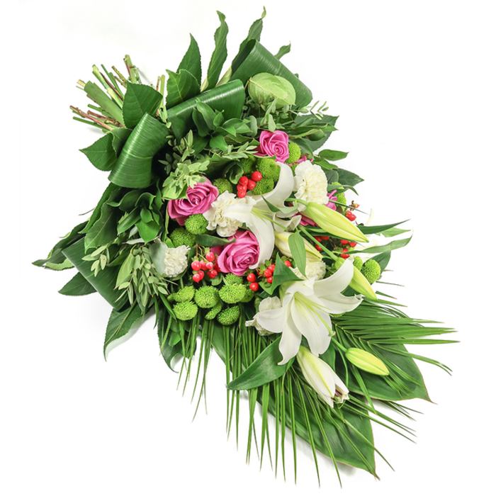 Meticulously composed against a white backdrop, this diagonal funeral floral spray from Brent Cross is a study in harmony and elegant contrasts. Open and budding white oriental lilies claim centre stage, their pristine petals unfolding with delicate gold-dusted stamens to radiate purity and serenity. Interlaced with these classic blooms are plush pink roses of varied sizes, opening to reveal graceful spirals and a touch of heartfelt sentiment. Filling the spaces are clusters of white spray carnations, their softly ruffled edges lending gentle volume and cloud-like texture. Bright green button chrysanthemums offer a lively, modern accent, reminiscent of renewal after spring rain at Brent Reservoir. Pops of vivid red hypericum berries provide both visual contrast and a sense of cheer. Anchoring the bouquet, an abundance of glossy, deep green leaves-some sculpted, others more naturally flowing-combine with feathery sprays and long, arching palm fronds that cascade through the design, bringing both structure and gentle motion. Every aspect of this arrangement is carefully curated for funeral and memorial gatherings in Brent Cross, offering a meaningful gesture of condolence and comfort, delivered thoughtfully to homes and services throughout the area.