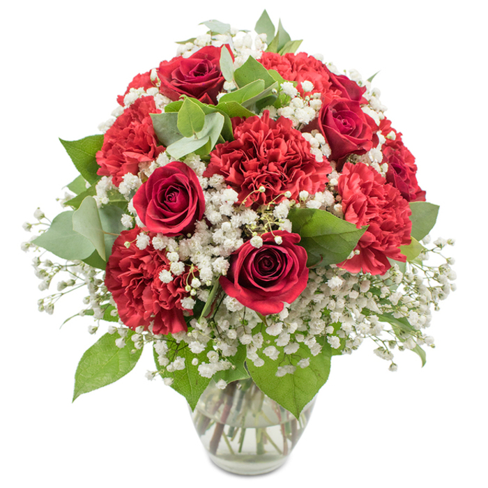 A striking bouquet of red and white flowers is captured in a clear glass vase against a bright white background, the kind of polished design a local florist might prepare for same-day delivery around Brent Cross. At the centre of the composition, several deep red roses stand tall, their velvety petals spiralling inward in tight, elegant curls that convey classic romance and quiet intensity. Surrounding them, clusters of crimson red carnations add lush fullness; their layered, finely fringed petals create a rich, textured surface that invites the eye to linger. Between these bold red forms, a veil of white baby's breath softens the arrangement, the countless small, airy blooms filling spaces like gentle puffs of cloud, bringing brightness and a sense of light-hearted purity that balances the deeper tones. Sprigs of fresh greenery, including the darker rose foliage and rounded eucalyptus leaves in cool, silvery hues, thread through the bouquet, adding depth, contrast, and a subtle nod to the leafy corners of nearby parks and residential streets off Hendon Way. The overall shape of the bouquet is a smooth, rounded dome, densely packed and thoughtfully proportioned so that every angle feels full and harmonious, as if just set on a table in a Brent Cross home for an anniversary dinner or special celebration. The clear glass vase has clean lines and a slightly flared rim, its transparency revealing neatly cut stems immersed in clear water, a mark of expert preparation and attention to lasting freshness. Bright, even lighting illuminates the arrangement, intensifying the reds, crisping the whites, and giving the greens a soft sheen. The scene exudes warmth, intimacy, and quiet festivity, ideal for Valentine's Day, milestone celebrations, or sending a heartfelt message of love and appreciation across Brent Cross and the surrounding neighbourhoods.