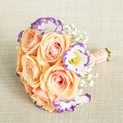The craftsmanship of this bouquet radiates the warmth and serenity of Brent Cross, as full apricot and blush-pink roses unfold leafiest petals against the soothing background of textured cream linen. Each bloom's pastel peach tone glows softly, conjuring the gentle light of a peaceful afternoon stroll through areas like Watling Park. White lisianthus, their petals edged in vibrant violet, dance between roses, infusing the arrangement with a vivid, painterly contrast that recalls the lively colour of local shops near Hendon and Temple Fortune. Baby's breath drifts among the flowers, its delicate, cloud-like clusters bridging the design with traditional charm. The hand-tied stems are finished in a lustrous peach-pink ribbon and tastefully accented with petite pearl beads-an elegant flourish reminiscent of family gatherings near Brent Cross Shopping Centre. This bouquet is crafted for cherished moments big and small-ideal for clutching as a bridesmaid, gracing a registry table, or adorning homes celebrating new beginnings in North West London. Every element reflects the care and creative vision typical of a skilled Brent Cross florist, blending time-honoured beauty with a dash of contemporary style.