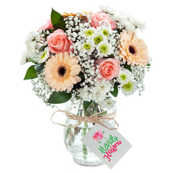 Bright and serene, this charming bouquet from Brent Cross conjures images of sunlight spilling across nearby Clitterhouse Playing Fields. Plush peach-pink roses, gently unwinding in soft spirals, share the spotlight with two spacious gerbera daisies in shades of peach and orange, their energetic tones matched perfectly to the spirit of the neighbourhood. Billowy sprigs of baby's breath wind between, softening the lines and creating an ethereal backdrop that lets each bloom shine. Clusters of crisp white chrysanthemums with lively lime centres lend a clean, invigorating finish-like the first breath of fresh air on a morning stroll down Highfield Avenue. Eucalyptus foliage is sparsely placed, its deep green leaves accentuating the bouquet's brightness with subtle depth and a cooling herbal scent. The ensemble is presented in a clear glass vase, subtly textured with elegant curves and filled with fresh water, the stems gathered in sturdy alignment. Around the neck, a natural raffia ribbon is neatly tied, finished with a classic white tag-blank for a message from sender to recipient. This bouquet's gentle beauty and sense of occasion make it ideal for celebrating new beginnings or delivering a warm gesture of support within the Brent Cross community.