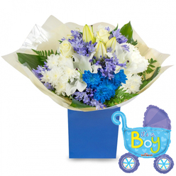 This bouquet reads like a lullaby in flowers-a quiet, joyful announcement for a newborn boy set against a bright white backdrop that lets each bloom breathe. The heart of the arrangement is a compact, rounded gathering of pristine white roses, ivory lilies (some still in bud as a gentle symbol of new beginnings), and full spray chrysanthemums whose soft fringed petals create a cloudlike volume. Interspersed are bold, electric-blue chrysanthemums and a concentrated cluster of vivid blue florets that form an arresting focal point, while skeins of pale lavender or periwinkle hyacinth-like blooms impart a subtle, powdery texture. The greens are thoughtful and textural: deep glossy leaves counterpointed by delicate ferny fronds, their scent faintly green and comforting when the bouquet is unwrapped. The flowers are wrapped in soft, crinkled cream tissue that gathers at the base and sits inside a sturdy, matte royal-blue rectangular box-an elegant contrast of deep tone and soft petal. A jaunty foil balloon shaped like a vintage pram floats to the right, its pale-blue surface decorated with darker-blue trim, polka dots and hearts, and the words "It's a Boy" rendered in playful yellow and green. This composition feels hand-tied by someone who knows local tastes-a perfect welcome for a son arriving in Brent Cross, suitable for a hospital bedside, a baby shower at a nearby community hall, or a heartfelt doorstep surprise in the surrounding neighbourhood.