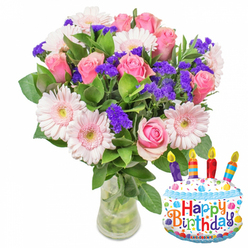 Bathed in clean daylight against a white backdrop, this birthday bouquet reads like a quiet celebration - elegant, joyful and carefully composed by hands that know how colour and texture sing together. The focal point is a full cluster of pink roses, each bloom at a different stage of opening so the tones shift from whisper-soft blush to a warmer, rosier pink that invites touch. Encircling those roses are pale pink Gerbera daisies, their broad, layered petals pale almost to ivory at the edges, centers warmed with a pale yellow that brightens the composition like a smile. Interwoven throughout are sprays of vivid purple statice or limonium; their small, papery clusters add a crisp, unexpected texture and deepen the palette so the pinks read richer. Tiny white filler blossoms peek through, adding flecks of light, while a generous complement of glossy, deep green foliage holds the bouquet with a natural, garden-like silhouette. The flowers sit in a clear glass vase with a gently flared base, the stems submerged in clear water that suggests recent conditioning and freshness. To the lower right, a playful metallic cake-shaped balloon complements the arrangement - rendered in white with blue piped icing, a scatter of multi-coloured sprinkles, and four striped candles in purple, red, orange and blue with small yellow flames. Across the cake a cheerful "Happy Birthday" is printed in bright, multicoloured letters; at the very bottom of the balloon the tiny brand name "KALEIDOSCOPE" is visible. The overall impression is one of considered cheerfulness - a fragrant, tactile gift that would suit a neighbour in Brent Cross or a friend picked up after coffee at the nearby shopping centre, ready to mark a birthday with colour and warmth.