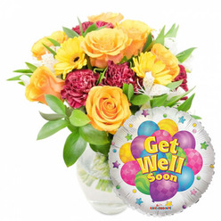 Sunlit and reassuring, this cheerful get-well bouquet reads like a small promise of brighter days. At its center several velvety yellow-orange roses open in generous spirals, their petals suggesting a light, citrus-tinged fragrance that lifts the composition; as a florist in Brent Cross I picture the flowers arriving fresh from local markets and being conditioned so their scent and shape remain true. Bright yellow gerbera faces break the surface with their sunny roundness, while rich burgundy or magenta carnations tumble between blooms, their ruffled texture offering a tactile contrast against the smoother rose petals. Sprays of small white alstroemeria thread throughout the arrangement, introducing points of delicate light and air, and the whole is framed by lush, glossy greenery that cradles each stem. The bouquet rests in a clear glass vase where stems and water are visible - the simple vessel keeps the focus on colour and freshness. Nestled to the lower right and slightly overlapping the flowers, a silvery Mylar balloon adds whimsy: a playful cluster of printed balloons in blue, purple, pink, yellow and green sits at its center, some striped, some with polka dots, encircled by tiny starbursts on the white border. Cheerful yellow-and-blue lettering reads "Get Well Soon," and a small "KALEIDOSCOPE" mark sits at the bottom rim. The overall impression is bright, tender and reliably hopeful - an ideal pick-me-up for someone recovering at home or in hospital in Brent Cross, Cricklewood or nearby parts of north-west London; Brent Cross Flowers can prepare and deliver this thoughtful arrangement within the local area.