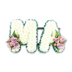 A serene and heartfelt floral tribute forms the word MA in bold capital letters, beautifully suited to honour a cherished mum, mama, or grandmother. Every inch of the letters is covered in tightly clustered white chrysanthemums, so densely arranged that they resemble a soft, cloud-like blanket of petals. The uniform whiteness of the blooms suggests purity and reverence, while their gentle, rounded shapes add comfort and warmth to the design. Around the outer edges, a deep emerald green satin ribbon is meticulously folded into neat ruffles, following each line and corner of the M and the A with careful precision. This pleated border frames the white flowers and gives the letters a clear, defined outline that stands out against the neutral backdrop. A slim connecting bar, mostly hidden behind the blossoms, links the two letters, helping them appear as one cohesive tribute. At the bottom of the M's left side and the A's right side, matching floral clusters offer a hint of soft colour. Pastel lilac roses, pale pink roses, and small pink spray roses are gathered together, their velvety petals opening gently in layered spirals. Fern fronds and fresh foliage tuck in between the roses, lending contrast and a light, airy feel. The tribute is displayed on a simple white background, making each detail of the flowers and ribbon visible and uncluttered. It is easy to imagine this arrangement resting beside the coffin or at the front of a chapel in Brent Cross, perhaps for a service near the shopping centre or local synagogues, offering a dignified and loving farewell.