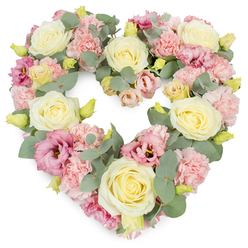 A tender, heart-shaped funeral tribute fills the image, meticulously crafted in soft pastel shades and set against a clean white background that gently amplifies the colours. The heart is entirely covered with flowers, creating a lush, full appearance that conveys generosity and care. At the core of the design are several creamy ivory and pale yellow roses, their spiralled centres and smooth, velvety petals opening outward in calm, rounded forms. Interspersed between them are clusters of ruffled light pink carnations, whose frilled edges introduce a delicate, almost feathery texture to the wreath. Deeper pink and mauve lisianthus blossoms appear at intervals, their slightly more open, trumpet-like petals and occasional darker centres offering a subtle contrast, like quiet moments of deeper emotion amid gentler tones. Sprigs of silvery eucalyptus, with their rounded, muted green leaves, weave through the flowers and trace the outline of the heart, lending structure, depth, and a cool freshness that tempers the warmer shades. Tiny yellow-green buds are tucked throughout the design, adding a sense of youth and renewal to the tribute. The overall palette of creams, blush pinks, soft yellows, and silver-green foliage feels peaceful and contemplative, ideal for expressing sympathy and remembrance at funerals, cremations, or memorial gatherings around Brent Cross, Cricklewood, and Finchley Road. It is the sort of arrangement Brent Cross Flowers might prepare for families who want a refined yet deeply personal floral gesture-something that honours a loved one with quiet beauty instead of overt drama.