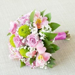 Arranged with a florist's gentle intuition, this bouquet brings to mind the promise of spring mornings in Brent Cross. Pale lilac-pink roses bask in soft light, their velvety petals almost crystalline, setting a tone of innocence and heartfelt emotion. Cheerful lime-green button chrysanthemums punctuate the blush tones, their playful roundness adding an uplifting contrast reminiscent of the lively greenery in and around Brent Cross's parks. Pink alstroemeria, lightly dusted with freckles, weave between the roses and chrysanthemums like thoughtful brushstrokes, echoing the creative spirit of local artisans. Drift-like clouds of gypsophila nestle within the bouquet, softening the arrangement and providing a tactile, dreamy presence-much like the early-morning mist that sometimes settles on local greens. The structure is completed by elegant dark green foliage, wrapping the bouquet in a frame of natural vitality. At the base, a satin-finished magenta ribbon secures the stems, expertly tied yet allowing the natural ends to remain visible, keeping the design rooted and genuine. Captured in gentle, even light, each bloom glows with freshness. This bouquet-a favourite for weddings and special occasions in the Brent Cross area-feels like the fresh air after a spring rain: a tangible celebration of hope and tenderness, expertly crafted in the heart of North West London and perfect for delivery to any event or doorstep nearby.