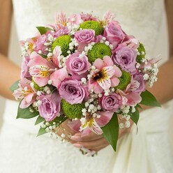 Within this striking bouquet, tradition and modern flair find harmony-echoing the vibrant yet tranquil atmosphere of Brent Cross. Nestled amid the lacy folds of a wedding gown, lush roses bloom in gradients of blush pink and lavender, their scent calling to mind the gentle perfume of spring mornings along Prince Charles Drive. Adding lively contrast, spherical lime green button chrysanthemums energize the bouquet with crisp texture and brightness, evoking the vitality of Henlys Corner. Subtle yet alluring pink alstroemeria lilies, with their streaked golden and berry centers, peek from the bouquet's heart, recalling the diversity and color that characterize Brent Cross shopping days. Wispy sprays of white baby's breath fill the spaces, floating between petals like soft clouds and giving the design a dreamy lightness. Framed by deep green, glossy leaves, the bouquet is expertly arranged, with each flower chosen for freshness and impact by Brent Cross Flowers. The overall effect is youthful and refined-perfect for modern weddings across North West London, and a celebration of life's most heartfelt moments, whether exchanged near Brent Cross Shopping Centre or within the leafy surroundings of Temple Fortune.