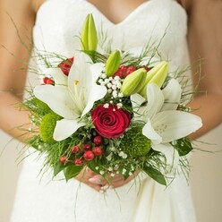 A bouquet where craftsmanship, emotion, and locality unite-a wedding favourite among Brent Cross couples. Featuring pristine white lilies whose broad petals glisten softly, the bouquet exudes innocence and clarity, mirroring the fresh morning air of Brent Park. At the core, deep crimson roses swirl tightly, their richness lending gravitas and warmth, while accents of bright red hypericum berries pulse with uplifting energy. Unopened green lily buds stand out, suggesting hopeful anticipation, as gentle sprays of gypsophila add a light, floated texture. Spherical green buttons and verdant ferns bring movement and intrigue, layering tactile pleasure from satiny blossom to cool, feathery touch. Everything is arranged for heartfelt beauty, intended to evoke lifelong memories for a bride surrounded by loved ones in Brent Cross. The composition feels both curated and natural, an ode to romantic tradition and the lively rhythm of North West London, making it a stellar choice for local weddings or event planning with Brent Cross Flowers.