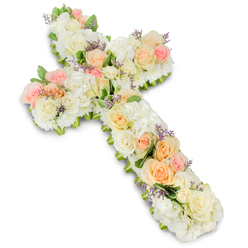 An exquisitely arranged floral cross takes centre stage, shown in full length against a clean white backdrop that highlights both its sacred outline and the delicacy of each bloom. The cross is entirely cloaked in fresh flowers, with no visible stems or framework, giving the impression of a soft, abundant cushion of petals shaped into a Christian symbol. The primary colour palette is calm and tender: white and ivory roses and fluffy hydrangea heads create a luminous base, their petals layered in generous, overlapping whorls. Intertwined with these are pastel roses in muted peach, soft apricot, and gentle blush pink, artfully placed so that pockets of warm colour appear to glow along the vertical and horizontal arms of the cross. Smaller, tightly clustered spray roses and filler blossoms fill every gap, creating a dense, luxurious texture that invites the eye to travel slowly over the surface. Here and there, discreet hints of lavender or light purple filler flowers emerge, giving a delicate lift to the design and adding subtle contrast. A narrow halo of fresh green foliage outlines the cross, reinforcing its form and providing a refreshing edge of colour without hardening the soft silhouette. The bright lighting and white background lend a sense of purity and calm, while a faint shadow gives the cross gentle depth. It is easy to imagine this tribute resting by the altar of a church near Brent Cross tube station or at a memorial gathering along the Edgware Road, created by Brent Cross Flowers as a heartfelt gesture of condolence, faith, and gratitude for a life remembered with love.