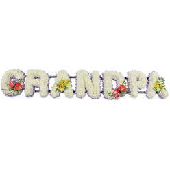 Set against a plain white background, a long floral display spells out the word GRANDPA in bold capitals, each letter fully encrusted with small white chrysanthemums. The petals form a plush, velvety layer of white, with each bloom nestled closely into the next so that no foliage or gaps appear, giving the impression of a continuous, cloud-like surface. Around the foot of every letter runs a slim trim of pale lavender ribbon, glimpsed beneath the flowers as a soft lilac outline. This gentle halo of colour adds definition and a hint of calm coolness, while the letters themselves are fixed to narrow dark green bars that hold the entire piece securely together, ready to be placed in a church or crematorium serving families from Brent Cross and the surrounding North London areas.   

Touches of vivid colour have been designed to personalise the tribute for a beloved grandfather. On the 'G' and the 'D', rich red anthuriums create striking accents; their heart-shaped, waxy spathes sheen subtly in the light, while their golden-yellow spadices stand prominent at the centre. These sit within clusters of deep green foliage and a scattering of tiny purple filler flowers, adding depth and contrast. The first 'A' and the final 'A' are adorned with sprays of yellow-green orchids, their graceful petals and intricate markings arranged among fresh leaves, lending a sophisticated and contemporary feel. The tribute speaks of steady love, cherished memories, and quiet strength, a floral GRANDPA sign that would feel at home at a funeral service or graveside gathering in Brent Cross, offering comfort when words alone are not enough.