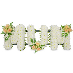 This image shows a beautifully composed MOM funeral tribute laid out horizontally, the three capital letters standing out crisply against a seamless white background as though floating in soft light. Each letter is formed on an unseen framework and completely blanketed with small, delicate white blossoms-most likely spray chrysanthemums or similar blooms-packed so closely together that they create a thick, cushiony texture. The petals overlap in layers, giving a velvety, cloud-like effect that conveys purity and calm, just the sort of arrangement that might be placed beside a coffin in a Brent Cross funeral home or delivered to a chapel near the shopping centre. Around the outer edges of the letters, a faint line of dark green frame and ribbon is visible, providing just enough contrast to define the graceful shapes without distracting from the flowers themselves.   Soft colour is introduced through three floral focal points of peach and apricot spray roses. One cluster of roses decorates the upper left arm of the first M, the second rests gently at the base of the central O, and the third graces the upper right arm of the final M, giving a sense of balance and rhythm across the tribute. The roses vary from tight buds to half-open and fully open blooms, adding visual interest and a feeling of life and unfolding stories. Around each group of roses, small tufts of greenery-light, ferny textures mixed with firmer, darker leaves-spill out slightly over the bed of white flowers, bringing a soft, natural feel. The overall impression is of a lovingly crafted, personal farewell, perfect for families across Brent Cross, Cricklewood, and Finchley who wish to honour a devoted mother with grace and gentleness.