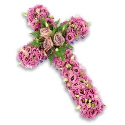 A beautifully composed floral cross arrangement rests against a pure white backdrop, the soft shadow behind it emphasising its depth and sculpted form. Crafted in tender shades of pink, mauve, and lilac, the cross has a gentle, contemplative presence that would feel at home at a memorial gathering near Brent Cross. The surface is densely packed with lisianthus blooms, each with slightly ruffled petals that overlap like fine fabric, creating a plush, almost quilted effect down the vertical stem and along the horizontal arms. The colour palette transitions from delicate blush and pale rose to deeper, more saturated pinks and lavender tones, with some flowers showing darker centres that offer subtle contrast. At the exact midpoint where the arms intersect, three open roses in dusty rose or soft mauve tones form a central feature, their layered petals unfurling in graceful spirals. These roses are framed by sprays of fresh green fern and smaller, darker leaves, which introduce a cooling, garden-fresh note to the design. Throughout the cross, tiny pink and purple accent flowers, along with small cream and white blossoms with yellow centres and a few tender green buds, are interwoven among the main blooms, giving a sense of natural rhythm and fine detail. Around the outline of the cross, especially along the outer edges, slender bands of deep purple ribbon or supportive material occasionally peek through, discreetly reinforcing the shape. The arrangement feels dignified yet gentle, reminiscent of a thoughtfully chosen tribute arranged by local Brent Cross florists for a church service or cremation, offering a visual expression of faith, remembrance, and quiet compassion for the family.