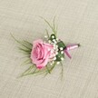 A delicately crafted pink rose boutonniere is laid out on a softly textured, light beige linen cloth, the weave of the fabric gently visible and giving the scene an organic, Brent Cross townhouse feel. At the centre rests a single blush-to-rose-pink bloom, its velvety petals spiralling out from a slightly tighter heart to edges that curl open in full, romantic freshness. The colour moves from a pale, almost shell-pink at the core to a richer, deeper pink at the petal tips, as if catching the last warm light over nearby Clitterhouse Playing Fields. Clusters of tiny, cloud-like white baby's breath gather around the base of the rose, their small, pearl-sized florets softening the design and adding a whisper of traditional wedding charm. Wispy, grass-like strands of light emerald foliage fan gently from behind, while a broader, darker green leaf is neatly folded to cradle the stems, giving the piece structure and polish. The stems are wrapped in a smooth satin ribbon that blends lavender-pink with a more saturated magenta tone, tied in a compact, tidy knot with short trailing ends that rest against the linen. Soft, even lighting casts subtle shadows that emphasise the rose's layered texture and the baby's breath's airy volume, making the boutonniere appear freshly prepared for a groom, groomsman, or prom date stepping out around Brent Cross. The overall mood is refined yet tender, the kind of handcrafted detail a local florist would create for intimate ceremonies, registry office weddings, or special celebrations that call for understated romance and carefully balanced colour.