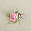 Displayed on a softly textured, light beige surface that looks like woven linen, this pink rose boutonniere exudes the quiet refinement often chosen by couples marrying near Brent Cross and the leafy streets around Hendon. The rose sits at a slight diagonal in the lower left portion of the frame, its petals closely nested in a graceful spiral. The outer petals show a vivid magenta-pink hue, while the colour gradually fades into a delicate pastel blush at the tightly furled centre, creating a natural ombré effect that makes the flower appear luminous. Around the rose, tiny white blooms of baby's breath are artfully placed, forming light, airy clusters that soften the composition and bring a cloud-like texture. Long, slender strands of grass-like greenery extend outward from behind the main bloom, providing a subtle sense of movement, as though the boutonniere had just been lifted from a cool florist's bench. At the base, a broader emerald green leaf curls protectively around the stem, its surface freshened with a few glistening droplets of water that add a hint of sparkle. The stems of the rose and foliage are bound together in a smooth, pale pink satin ribbon, wrapped neatly in even coils that show careful hands at work. The design concludes with a slim bow in a deeper magenta-pink ribbon, harmonising with the darker edges of the rose petals and giving a refined two-tone finish. The neutral background means every colour and texture stands clearly on its own. This boutonniere would sit beautifully on a groom's or usher's lapel for a Brent Cross ceremony, radiating romance, tenderness, and meticulous floral artistry.