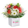 This uplifting bouquet, nestled within a clean white gift bag, gives the impression of sunlight and celebration-a tribute to Brent Cross's vibrant pulse. Fluffy coral and peach carnations ripple through the arrangement, joined by bursts of vivid red, every petal soft and ruffled like the inside of a secret garden. Fresh white daisies, their golden-green eyes twinkling, peek cheerfully from among the bolder colours, carrying a gentle fragrance and a sense of innocence. Wisps of delicate baby's breath float among the other flowers, lending an ethereal, cloudlike quality that catches the light, much like soft morning mist over Brent Reservoir. Glossy, deep green leaves provide contrast and structure, cradling the blooms and highlighting their fullness and symmetry. On one side, unopened buds tinged in violet suggest the hopeful beginnings of something beautiful. The sturdy ribbon handles atop the pristine white bag make this ensemble perfect for easy gifting-whether as a surprise for a special occasion or a spontaneous burst of happiness delivered across Brent Cross. Composed with care and expertise, the bouquet reflects the artistry and heartfelt spirit of the local community, capturing the delight and optimism that fresh flowers bring to every gathering.