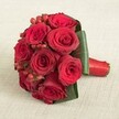 A glorious hand-tied bouquet of deep red roses sits poised atop an elegant textured linen, ready to grace a Brent Cross celebration. Each rose-full, radiant, and velvety-uncurls with flawless precision, creating a dense, rounded composition suffused with an air of passion and grace. Scattered amidst the red blooms, glossy clusters of bright hypericum berries pop with festive charm, while sweeping green leaves hold and sculpt the bouquet into its refined, compact shape. The stems are expertly bound in rich red satin, forming a seamless and comfortable grip-a point of craftsmanship appreciated by Brent Cross residents celebrating at home or at Edgware Road venues. Light falls across the arrangement with subtle evenness, revealing the lustrous surfaces and intricate textures of every element. This bouquet from local florists is more than just a gift; it's a lasting emblem of romance and artistry, making the perfect centrepiece for a bridal processional, a milestone anniversary, or an authentic expression of love delivered anywhere in the wider Brent Cross neighbourhood.