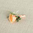 In the morning's soft, diffused light this peach rose boutonniere offers a study in refined understatement, the kind of small composition that quietly anchors a suit jacket at a wedding or anniversary. At its centre the rose opens in warm apricot tones that sink into a gentler peach at the petal margins; the petals' velvet surface catches and holds light unevenly, giving the bloom depth and the impression of movement. Tiny clusters of baby's breath punctuate the arrangement like distant stars, their minuscule white blossoms adding air and innocence that balance the rose's richness. Deep green blades and curled glossy leaves provide a cool, structured contrast - their smooth, slightly waxy surfaces a tactile foil to the rose's soft nap. The stem is bound in a satin ribbon in a matching peach hue, wrapped and finished with a small, tidy bow whose faint sheen catches a glint of light. Resting on neutral linen, the whole boutonniere reads as carefully considered and expertly finished, ideal for intimate ceremonies in Brent Cross, small receptions near Cricklewood or celebratory walks around the nearby green spaces. As a local florist I find this piece speaks to moments of gentle pride and close celebration: it photographs beautifully, holds to the lapel without fuss, and leaves an impression of warmth and restraint that feels both current and classic.