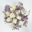 From a top-down perspective, this photograph captures a round, softly balanced bouquet of white roses and lavender limonium, positioned against a spotless white background that underscores its calm, contemplative mood. The central focus is a compact grouping of about twelve white roses, each bloom nestled closely to the next. Some are still in bud, with petals wrapped neatly and smoothly, while others are beginning to open, petals curling outward in gentle spirals. A few roses are fully open, revealing their layered, rosette-like hearts, where creamy white petals subtly deepen to touches of ivory or pale lemon at the very base. Interwoven among the roses are numerous sprigs of limonium, carrying clusters of tiny lavender-purple flowers that form a light, cloud-like frame around the larger blooms. These delicate filler flowers add a fine, intricate texture and introduce a soft veil of colour, contrasting with the broad, velvety petals of the roses. Small slivers of green stem and minimal foliage are visible here and there, discreetly supporting the arrangement and adding a hint of natural freshness. The overall design is refined, pure, and soothing, ideal for moments of farewell or quiet remembrance. In Brent Cross, a bouquet like this might be chosen for same-day sympathy delivery to a family along Hendon Lane, or placed at a modest graveside service nearby. It carries a message of peace, respect, and enduring love, allowing its gentle whites and lavenders to offer solace when comfort is needed most.