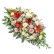 The photograph shows a refined double-ended coffin spray laid against a sharp white background, its colours and textures captured in crisp detail. The arrangement is long and gently tapered, symmetrical enough to feel balanced yet soft enough to appear organic, as if it has been shaped by a caring hand for a farewell in Brent Cross. Deep red Oriental lilies, with their dramatic, star-shaped petals and slightly curved tips, rise above the surrounding blooms as bold points of emotion and remembrance. Around them, a generous scattering of roses in cream, ivory, and blush pink creates a sense of quiet romance, their layered petals catching the light and giving the spray a plush, luxurious look. Ruffled pale pink carnations and clusters of white spray chrysanthemums fill the interior, ensuring a full, abundant appearance with no visible gaps, just a continuous tapestry of soft colour. Peeking between the larger flowers are delicate touches of lavender and light purple filler stems, together with a few sculptural, steel-blue thistle-like flowers that provide subtle contrast and a touch of contemporary style. The entire floral composition is underpinned by a lush array of dark green foliage-broad, glossy leaves and finer, feathery sprigs-that cradle the blooms and extend slightly beyond the edges, creating a gently undulating outline. The mood conveyed is one of respectful sorrow balanced with gratitude for a life well lived, like a floral embrace offered to mourners gathering near Brent Cross Shopping Centre or along the Edgware Road, thoughtfully arranged by an experienced local florist so that every stem contributes to a message of love, memory, and peace.