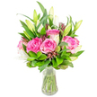 A vibrant, eye-catching bouquet of deep pink roses and white lilies sits in a clear glass vase, photographed against a clean white backdrop that brightens every petal and leaf. Several large roses, their velvety petals graduating from soft blush to richer fuchsia at the heart, form the warm centre of the arrangement; their layered textures invite a gentle inhale of a sweet, nostalgic rose perfume. Interwoven are elegant white lily buds, many still tightly furled and some just beginning to unveil their trumpet shapes, the faint green tips and emerging stamens hinting at future bloom. Surrounding the flowers is an abundance of fresh, glossy greenery - broad, pointed leaves alongside finer, lighter sprigs - which cushions each bloom and creates a lively, verdant frame. Small, darker burgundy or reddish-brown accent buds are scattered through the design, adding shadowed points of contrast and a pleasing tactile depth. The vase itself is simple and classic, a slightly flared rim and sturdy base holding clear water through which neatly cut stems are visible, their green shafts aligned like the stems you would prepare for delivery on a busy morning. Soft, even lighting suggests a bright studio or a north-facing window in a warm Brent Cross kitchen, where the colours would hold true and the scent would quietly fill the room. As a local arrangement that might be chosen for a birthday, anniversary, or a thoughtful 'just because' note, this bouquet captures both refined floral technique and approachable warmth, ready to be sent across Brent Cross, Cricklewood, or nearby Hendon to brighten a home or office table.
