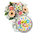 A bright, encouraging 'Good Luck' gift set captured against a clean white backdrop - a composition that radiates warmth and quiet celebration. To the left a generous bouquet sits in a simple clear glass vase, its neck tied with a natural twine bow; soft peach and pale pink roses form the heart of the arrangement, their petals tightly furled and smelling faintly of summer afternoons. Peachy-orange Gerbera daisies with deep chocolate-brown centers add cheerful, satiny texture, while airy sprays of white gypsophila (baby's breath) thread through like delicate lace. Small clusters of white and lime-green chrysanthemum florets bring crisp, bright accents and a hint of springy freshness, all set against deep green foliage that gives the bouquet depth and a natural silhouette. To the right, overlapping the lower portion of the vase, a round silver metallic foil balloon claims the foreground: the festive phrase Good Luck! blooms across its face in playful, multi-coloured letters, and the two o's are replaced by yellow smiley faces - one winking, the other sticking its tongue out - adding a mischievous, hopeful note. The balloon's silver surface is scattered with tiny stars, hearts and confetti-like shapes in blue, pink, yellow and orange, and a small KALEIDOSCOPE logo sits discreetly at the bottom. Soft, even lighting highlights the petals' velvety textures and the vase's glass clarity, making the colours sing without harsh shadows. This image feels like a small, hand-tied encouragement - the kind of thoughtful floral and balloon pairing you might send to someone starting a new chapter, facing exams, or stepping into a new job - simple, fresh and quietly celebratory for recipients across Brent Cross and neighbouring Cricklewood or Hendon.