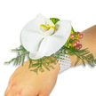 A pristine white Phalaenopsis orchid crowns an elegant wrist corsage resting on a fair-skinned wrist against a bright white backdrop. The orchid's broad, satiny petals unfold with a quiet, sculptural grace; at the centre a small, luminous labellum shows a warm wash of yellow and a deeper orange spot that reads like a tiny sunrise within the bloom. Beneath the flower, a soft bed of fine asparagus fern creates a lacy, feathered green frame, its delicate fronds drifting outward to give the composition air and movement. To the upper right a neat cluster of Hypericum berries adds a tactile counterpoint - glossy, round fruits graduating in colour from pale green through rose to rich cranberry, suggesting the gentle passage of the season. A ruffled spray of lime-green accent foliage nestles near the berries, bringing another whisper of texture. The whole piece is attached to the wrist by a classic multi-strand bracelet of small white pearls; the pearls catch the light with a cool, subtle sheen and sit comfortably against the skin, lending an heirloom calm to the design. The studio lighting is soft and even, the clean white background concentrating attention on surface, hue and form: the orchid's smoothness, the fern's filigree, the berries' gloss and the pearls' sheen. The overall mood is romantic and refined - a wearable nod to understated luxury suitable for a wedding, prom or special celebration. Locally made with seasonal flowers and available for delivery across Brent Cross and neighbouring Hendon and Cricklewood, this corsage reads as thoughtful craftsmanship and quiet celebration.