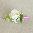 An elegant orchid boutonniere is laid gently on a neutral, linen-textured surface, the fabric's oatmeal tone providing a calm, natural backdrop that lets each floral detail stand out. At the centre sits a pristine white Phalaenopsis orchid, its petals broad, smooth, and subtly curved, almost like sculpted ceramic. Light falls softly across the bloom, catching the delicate yellow-orange and faint pink at its throat, where the intricate inner structure of the orchid draws the eye inward. Encircling this focal flower is a fine haze of tiny white Gypsophila, or baby's breath, each miniature blossom adding a sense of weightless volume, as though a small cloud has gathered around the orchid. Slim, fresh green leaves are woven into the design, their streamlined shape and glossy texture offering a clean contrast to the softly matte petals and airy baby's breath. To one side, three rounded, pale green orchid buds cluster along a thin stem, still closed but full and promising, symbolising moments yet to unfold-ideal for a wedding in Brent Cross, a prom near Hendon, or an intimate celebration by the shopping centre lights. The stem of the boutonniere is neatly bound with a bright pink satin ribbon, pulled tight for a tidy finish and tied into a compact bow whose short tails sit just beneath the flowers. The ribbon's sheen introduces a gentle pop of colour, playful yet sophisticated. Everything about the composition speaks of care and precision: the balanced proportions, the crisp contrast of white and green, the subtle movement created by the buds. It feels like a piece designed by a local florist who understands how a single flower on a lapel can carry emotion, memory, and the quiet confidence of a special day in North West London.