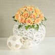 A hand-gathered dome of peaches and apricot roses rests atop an open, white-woven orb, its soft palette speaking of gentle celebration in the heart of Brent Cross. The roses are lush and abundant, each bloom shaped into a delicate spiral whose inner petals hold a whisper of cream while outer edges warm into apricot. Interspersed among them, clouds of white gypsophila drift like breath, their tiny blossoms catching light and lending an ethereal, almost veil-like effect. Sprays of deep green foliage provide contrast and structure, their cool tones grounding the softness of the petals and introducing a subtle, leafy fragrance.
The spherical rattan vessel has a contemporary, airy architecture: the white painted lattice throws soft shadows and lifts the floral dome visually, so the composition reads as both sculpture and bouquet. Sunlight glancing across the arrangement gives a pale golden glow, enhancing the peach hues and the powdery texture of the gypsophila. Perfect for a wedding, anniversary, or calm home styling, this piece conveys tenderness and refined craftsmanship - a design familiar to florists working around Hendon Way and the Brent Cross Shopping Centre. Prepared with careful hands and attention to seasonal freshness, this arrangement is available for local delivery by Brent Cross Flowers and makes a quietly confident statement of care and new beginnings.