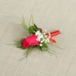 A single, exquisitely crafted boutonniere rests on a softly textured, light beige fabric that looks like natural linen, the neutral backdrop allowing every detail of the flowers to stand out with clarity. At its heart is a tightly furled fuchsia rosebud, deep pink petals wrapped closely together so the bloom feels full of promise, as if it might unfurl during a wedding ceremony in Brent Cross or a prom on a warm London evening. The rose's surface appears velvety and rich, catching the bright, even light and revealing subtle gradients of magenta and softer pink along the petal edges. Nestled around the central rose are airy clusters of tiny white baby's breath, each minuscule blossom forming a cloud-like halo that softens the intensity of the rose's colour. Behind and around the blooms, slender, feathery sprigs of bright green foliage, reminiscent of asparagus fern or ruscus, fan out in graceful arcs, giving the boutonniere an elegant, natural movement, as though it had just been gathered from a garden near Brent Cross Shopping Centre or Hendon Park. A slim, glossy red satin ribbon is wrapped neatly and tightly around the stems, the smooth fabric catching small highlights and adding a refined finishing touch that echoes the rose's passionate tones. The ends of the ribbon are tucked tidily, suggesting the careful hands of an experienced florist, and the whole composition lies at a slight diagonal, creating a gentle sense of energy and sophistication. This intimate floral piece suggests romance, celebration, and thoughtful craftsmanship, ideal for a groom's lapel, a groomsman, or a special guest attending a formal event or Valentine's dinner in the Brent Cross area.