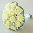 This softly luminous bridal posy, photographed on a light taupe fabric, is the kind of elegant simplicity we craft at Brent Cross Flowers for weddings across Brent Cross and the surrounding streets near the shopping centre. The arrangement centres on a compact, domed cluster of about fifteen to twenty creamy yellow roses, their petals unfurling in tightly packed spirals that read as both luxurious and tender. Sprays of delicate white Gypsophila are tucked between the roses like drifting mist, balancing the composition with an airy, romantic texture. Around the outside, long, slim leaves - possibly lily grass or bear grass - arch with a gentle architectural curve, forming an almost heart-shaped frame that guides the eye inward to the luminous rose faces. The natural green stems are visible at the base, precisely bound with a smooth white satin ribbon that adds a cool, tactile contrast to the warm bloom tones. The soft, diffused sunlight in the image reveals subtle gradations from creamy ivory to warm butter-yellow across the petals, and the faint, clean perfume of freshly cut roses seems almost present. The backdrop's muted weave enhances the overall feeling of calm and understated luxury, making this bouquet ideal for ceremonies from intimate registry ceremonies near Cricklewood to small church weddings sited close to Brent Reservoir. As a local florist, I choose materials and finishes here to convey trust, softness, and the quiet delight of a refined, timeless bridal bouquet.
