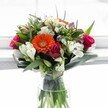 A lively bouquet, bursting with the colours of early spring near Brent Cross, glows in a simple, clear vase-its sunlit freshness lending warmth to any setting. Dominating the arrangement, a striking orange Gerbera daisy beams with positivity at the centre, held by a joyful mix of velvet-petaled magenta roses and soft white alstroemeria, their striped petals nodding gracefully. Dainty, white daisy chrysanthemums nestle amidst the blooms, adding light, feathery movement, while a handful of pale, buttery roses offer a note of softness and serenity. Glimpses of lavender and purple thread through the lush arrangement, creating a harmonious palette reminiscent of a stroll through Brent Cross' nearby parks. Generous greenery-broad, glossy leaves, and architectural spikes-cradle the bouquet, showcasing the artistry of Brent Cross Flowers and echoing nature's abundance. Bathed in morning light, with water-kissed stems visible in the vase, the bouquet feels as fresh as if straight from a local market, perfect for sending congratulations, celebrating milestones, or brightening a loved one's day in the heart of NW4.