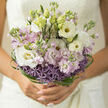 In this image, a hand-tied bouquet is held close, glowing softly as if it has captured the quiet light of a Brent Cross morning. The design is built around a gentle palette of pale blush, creamy white, and pastel lilac, with lisianthus and stock forming a cloud of velvety petals. The lisianthus blooms curl open in graceful layers, some fully unfurled and others still cupped, while the stock adds columns of tiny clustered flowers that rise between them, lending height and a faint, nostalgic sweetness. At the base, rounded heads of lavender allium form a subtle ring, each globe made up of fine, star-shaped florets that create a delicate, almost celestial texture. Encircling everything, fine strands of bright green bear grass weave and loop like calligraphy strokes, giving the bouquet a contemporary, almost architectural border reminiscent of the clean lines of the nearby shopping centre and surrounding streets. Natural light spills across the arrangement, heightening the contrast between the cool purples, warm whites, and vivid greens, so each blossom looks freshly cut, as if it has just arrived from a local grower ready for same-day delivery across Brent Cross and the neighbouring areas. Tender green buds are tucked throughout, hinting at blooms still to come and underscoring the feeling of hope and new beginnings. The bouquet feels light yet composed, ideal for a wedding, engagement, or romantic gesture, its quiet elegance reflecting the thoughtful craftsmanship of a florist who knows how to balance texture, colour, and scent in a way that will linger in the memory long after the petals fall.