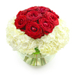 This image shows a refined floral arrangement of deep red roses and plush white hydrangeas, set in a clear, rounded glass vase and photographed against a clean white background, the kind of elegant centerpiece that would feel at home in a Brent Cross apartment or townhouse. The top of the design is formed by a compact cluster of about ten velvety red roses, grouped into a smooth dome. Each rose displays layered petals that fold and swirl around a central heart, some blooms just starting to open wider while others remain slightly tighter, giving the dome a subtle, natural variation. Encircling this crown is a lush, cloud-like base of creamy white hydrangeas, with countless small florets gathered into dense, rounded heads that create a beautifully soft texture. The hydrangeas spread outward in a full collar, gently supporting the roses and providing a luminous, neutral backdrop that makes the red tones appear even more vibrant. The clear glass vase below is shaped like a small fishbowl and is half-filled with clean water, clearly showing the fresh green stems arranged inside. Light reflects delicately off the curved glass and water surface, suggesting freshness and care in the preparation. There is no added foliage or decorative elements; instead, the focus remains on the striking simplicity of red and white. The overall look is polished and heartfelt, an ideal anniversary bouquet for delivery around Brent Cross, whether it is being sent to celebrate years together, decorate a dinner table near the shopping centre, or offer a quiet but powerful expression of love and gratitude.