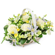 A softly composed funeral flower basket is displayed against a bright white background, its gentle colours and shapes conveying calm and consolation. The basket is woven from light-toned wicker in a soft beige or ivory shade, its slightly elongated form finished with a graceful handle arching neatly over the flowers. It looks comfortable and balanced, as though it could sit with ease on a table in a Brent Cross home or beside a framed photograph at a memorial gathering near the junction of the North Circular and Hendon Way. Inside the basket, the flowers are arranged into a smooth, rounded mound, filled so generously that no stems or gaps are visible. Large, creamy white roses take pride of place in the centre, fully open with velvety petals spiralling outward, giving a sense of serenity, honour, and heartfelt remembrance. Nestled between the roses are distinctive, star-shaped clematis in tones of pale lavender and soft periwinkle blue, their petals fine and slightly pointed, encircling vibrant yellow-green centres that glimmer gently in the light. Around these focal blooms, clusters of smaller white and pale yellow freesia-like flowers - some open, some still in slender buds - introduce delicate texture and the idea of a subtle, sweet fragrance. Tiny flickers of clear yellow flowers brighten the palette without disturbing its overall softness. The entire composition is embraced by lush green foliage, with broad, glossy leaves forming a strong base and smaller sprigs threaded through to add lightness and depth. The resulting effect is one of understated elegance and peace, perfectly suited for expressing condolences or honouring a loved one's memory in the Brent Cross area, where thoughtful, beautifully arranged flowers can help carry messages of support and care.