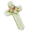 The image captures a reverent floral cross laid out against a spotless white background, its form defined by both colour and texture. The cross is completely clad in dense white chrysanthemum button flowers, each bloom carefully set side by side to create a plush, cushion-like surface. Seen as a whole, the cross appears as a solid expanse of white, suggesting purity and spiritual calm, the sort of mood that often surrounds quiet moments of reflection before a funeral or memorial gathering in Brent Cross or nearby Golders Green. At the intersection of the cross's arms and stem, a modest yet expressive cluster of roses introduces gentle pastel tones. Several roses, fully open to show their intricate whorls of petals, are arranged in shades of pale pink, creamy ivory, and warm peach. Around them, delicate fern fronds fan out just beyond the roses, their rich green adding depth, while fine sprigs of lavender or light purple filler flowers appear between petals, contributing a soft veil of colour. Along the very outer edge of the cross, a slim lime green ribbon runs continuously, only lightly revealed where the chrysanthemums lift, giving the piece a neat outline and a hint of freshness. The lighting is clear and even, casting a subtle shadow behind the arrangement that adds three-dimensional presence without overshadowing the design. This floral cross feels both traditional and personal, the kind of arrangement a family in Brent Cross might send to a church, crematorium, or graveside as a silent yet eloquent expression of sympathy, remembrance, and enduring faith.