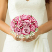 This wedding bouquet, held securely yet gently in the bride's hands, showcases a carefully structured dome of blush-pink roses surrounded by a mist of white gypsophila, the kind of romantic design often chosen by couples celebrating in and around Brent Cross. Each rose is open to its fullest, the petals soft and plush, overlapping to create rounded blooms reminiscent of finely folded silk. The pink tones are graceful and understated, with delicate gradations from deeper blush at the centre to creamy, almost ivory edges. Between these luxurious blossoms, clusters of baby's breath scatter countless tiny white flowers, adding a finely textured halo that softens the bouquet's outline, much like the gentle haze of early morning light over nearby Clitterhouse Playing Fields. The bouquet is hand-tied into a neat, spherical shape, suggesting classic bridal elegance and meticulous craftsmanship from a florist who knows the preferences of local brides. Gentle, natural light illuminates the scene, reflecting off the lace detailing of her gown and enhancing the contrast between the roses and the gypsophila, while slender shadows lend depth to the petals. Though you cannot smell it, there is an imagined perfume of fresh roses-light, romantic, and uplifting-following her steps as she walks through the venue. The overall impression is one of serenity, poise, and tender expectation, as if the bouquet were quietly holding all the emotion of the day. Ideal for weddings in Brent Cross, whether in intimate indoor spaces or nearby green settings, this arrangement feels like a subtle yet powerful symbol of commitment, devotion, and the gentle beauty of shared promises.