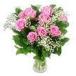 A graceful arrangement of pink roses and white baby's breath fills a clear glass vase, set before a clean white background that makes the colours and textures feel bright and immediate. The bouquet is composed of roughly ten to twelve pink roses in varying stages of bloom: some open wide to reveal their complex layers of velvety petals, while others remain gently cupped, hinting at freshness and the promise of more colour to come. The pink shades range from soft, baby-blush tones along the outer petals to slightly richer rosy hues at the centres, evoking warmth, tenderness, and the gentle joy of welcoming a new baby in Brent Cross. Threaded among the roses, feathery sprays of baby's breath carry clusters of tiny white flowers, creating a cloud-like softness that lightens the design and brings a sense of innocence and purity. Surrounding the blossoms, dark green rose leaves, smooth and slightly glossy, add a strong visual frame, making the pink and white flowers stand out even more vividly against the white backdrop. The transparent vase is simple and elegant, showing the neatly arranged green stems and the clear water inside, details that suggest professional floristry and freshly prepared blooms. Even, bright lighting highlights the subtle textures of each petal and leaf, avoiding harsh shadows so the bouquet appears calm and inviting. The overall effect is one of gentle celebration and cosy happiness, ideal for baby shower imagery, new-arrival announcements, or thoughtful floral gifts delivered around Brent Cross station, the shopping centre, and the surrounding family homes.
